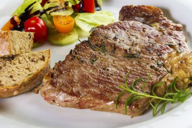Ev yapımı ekmek ve salata ile beyaz plaka üzerinde olgunlaşmış terbiyeli Dana but veya striploin biftek pişmiş