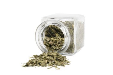 Beyaz arka planda izole edilmiş cam bir kavanozda kurumuş aşk otu. Baharatlar ve yemek malzemeleri.