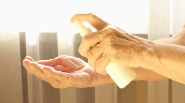 Yaşlı beyaz kadın Coronavirus covid-19 'dan korunmak için alkol spreyi kullanıyor.