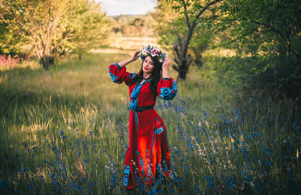 Beautiful young boho girl in ukrainian ethnic dress and a chaplet in a forest edge