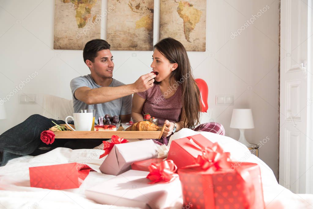happy couple having breakfast on bed with gifts celebrating valentines day