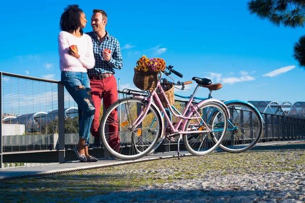 Happy young interracial couple enjoying a beautiful day by the river with their vintage bicycles — Stock Photo, Image