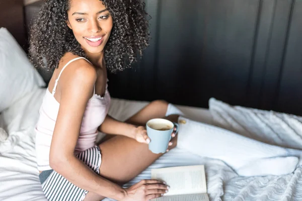 Woman reading a book and drinking coffee on bed with socks — Stock Photo, Image