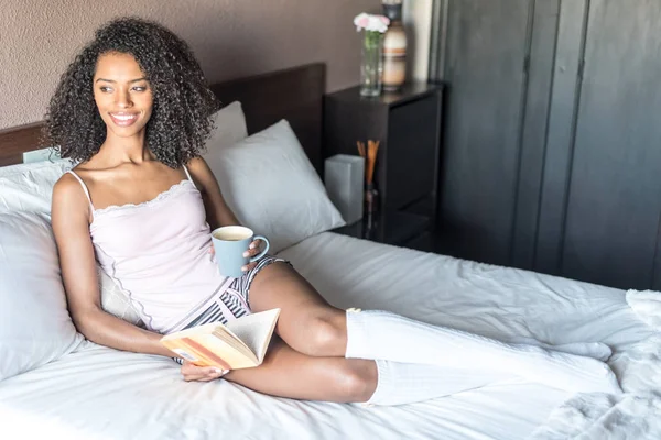 Woman reading a book and drinking coffee on bed with socks — Stock Photo, Image