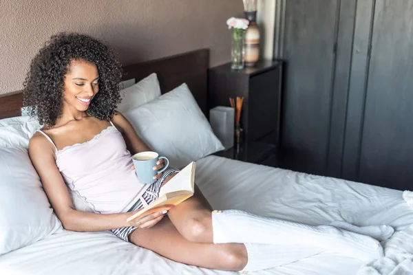 Mujer leyendo un libro y tomando café en la cama con calcetines — Foto de Stock
