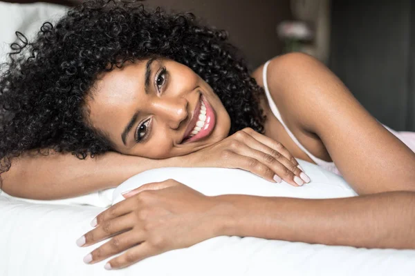 Negro mujer feliz en la cama sonriendo y estirándose mirando camer —  Fotos de Stock