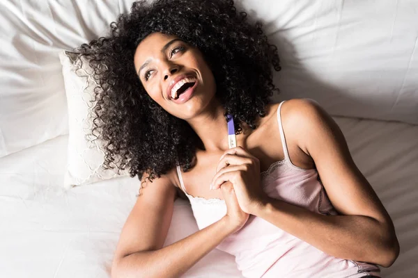 Mujer negra feliz con una prueba de embarazo en la cama — Foto de Stock