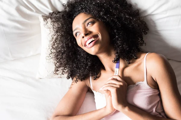 Szczęśliwy czarna kobieta z test ciążowy na łóżku — Zdjęcie stockowe
