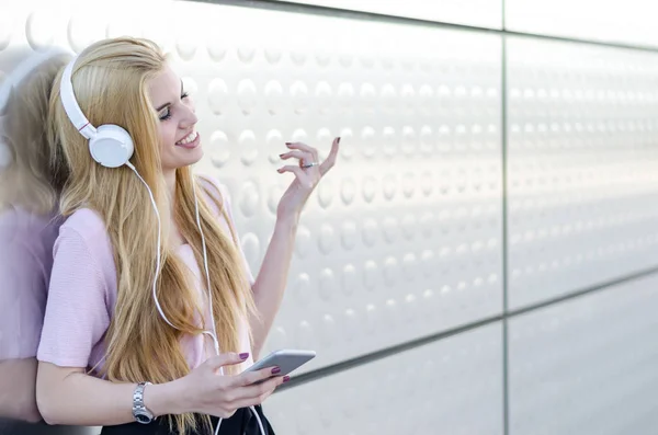 Mujer rubia escuchando música con auriculares y teléfono móvil al aire libre — Foto de Stock