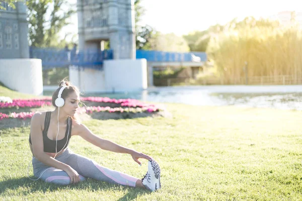 Kobieta robi ćwiczenia trawnik i rozciąganie na świeżym powietrzu w parku słuchania muzyki trawa sportowa — Zdjęcie stockowe