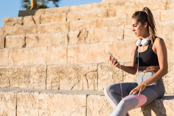 sports woman resting and listening music using her mobile phone in stairs