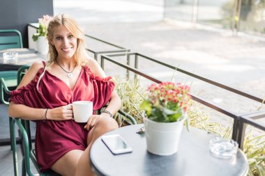 Güzel sarışın kadın bir teras bir fincan kahve içme.