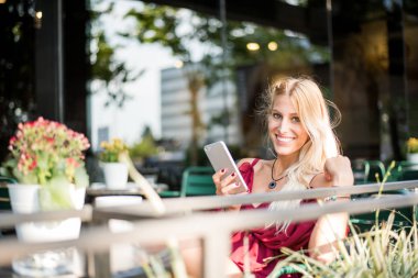 Mutlu sarışın güzel kadın bir terası açık havada bir fincan kahve içme bir cep telefonu kullanarak