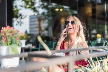 Mutlu sarışın güzel kadın bir terası açık havada bir fincan kahve içme bir cep telefonu kullanarak