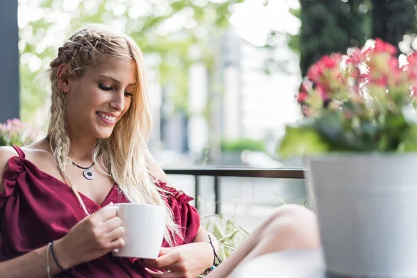 Όμορφη ξανθιά γυναίκα πίνοντας ένα φλιτζάνι καφέ σε μια βεράντα. — Φωτογραφία Αρχείου