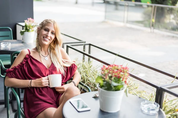 Beautiful blonde woman drinking a cup of coffee in a terrace. — Stock Photo, Image