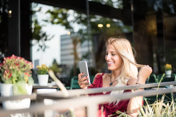Šťastné blond krásná žena pomocí mobilního telefonu, pít kávu na terase venku — Stock fotografie