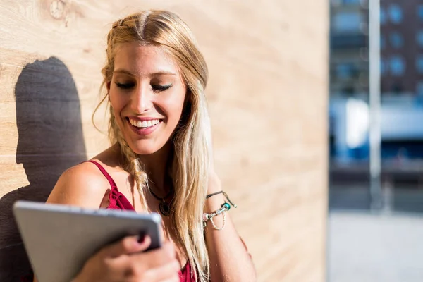 Mujer estudiante rubia feliz usando una tableta y sonriendo — Foto de Stock