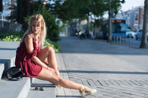 Heureuse femme blonde assise sur les marches de la rue portant une robe rouge — Photo