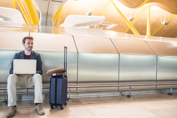 Joven hombre atractivo sentado en el aeropuerto trabajando con un lapto — Foto de Stock