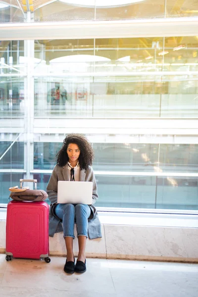 Mujer negra que trabaja con el ordenador portátil en el aeropuerto esperando en el wi — Foto de Stock