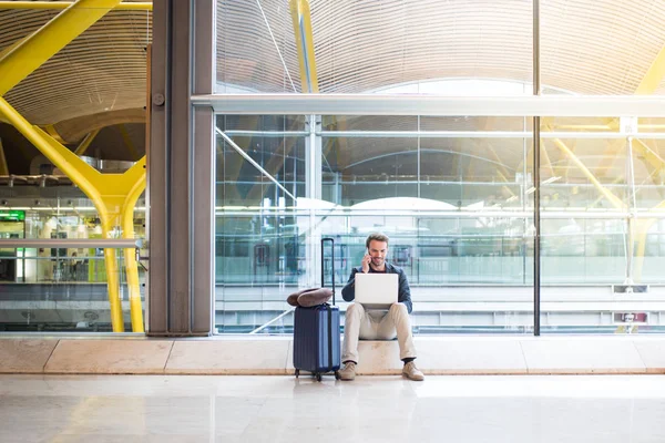 Homem sentado no aeroporto usando laptop e telefone celular ao lado de — Fotografia de Stock