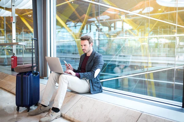 Man sitting at the airport using laptop and mobile phone next to — Stock Photo, Image