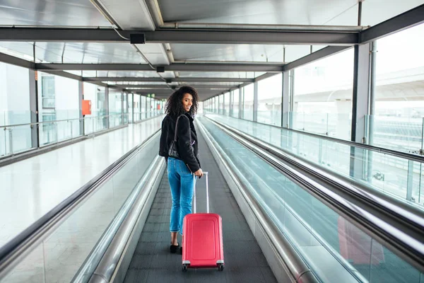 Mujer en la pasarela en movimiento en el aeropuerto con una maleta rosa . — Foto de Stock