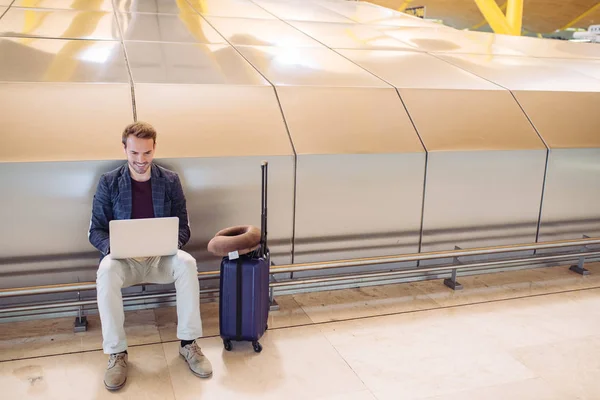 Jovem homem atraente sentado no aeroporto trabalhando com um lapto — Fotografia de Stock