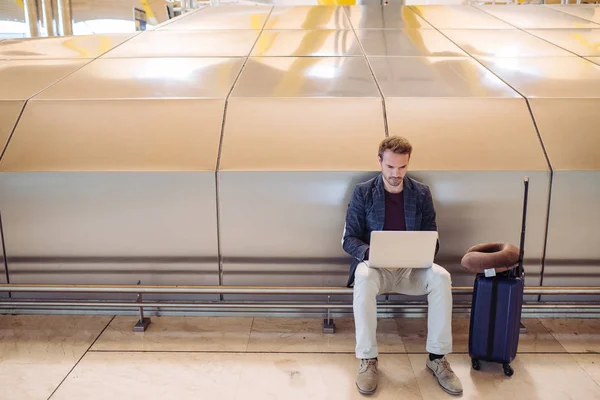 Junger attraktiver Mann sitzt am Flughafen und arbeitet mit einem Lapto — Stockfoto