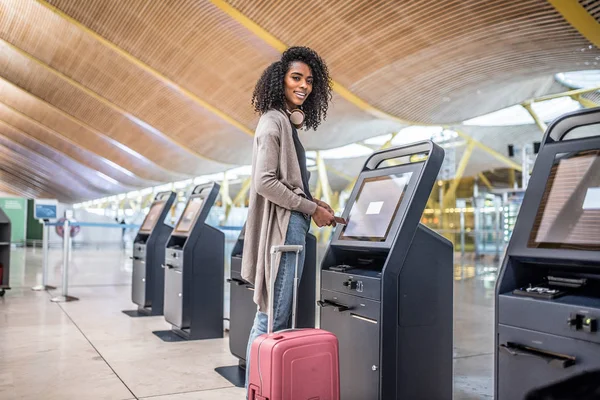Femme heureuse en utilisant la machine d'enregistrement à l'aéroport obtenir th Images De Stock Libres De Droits