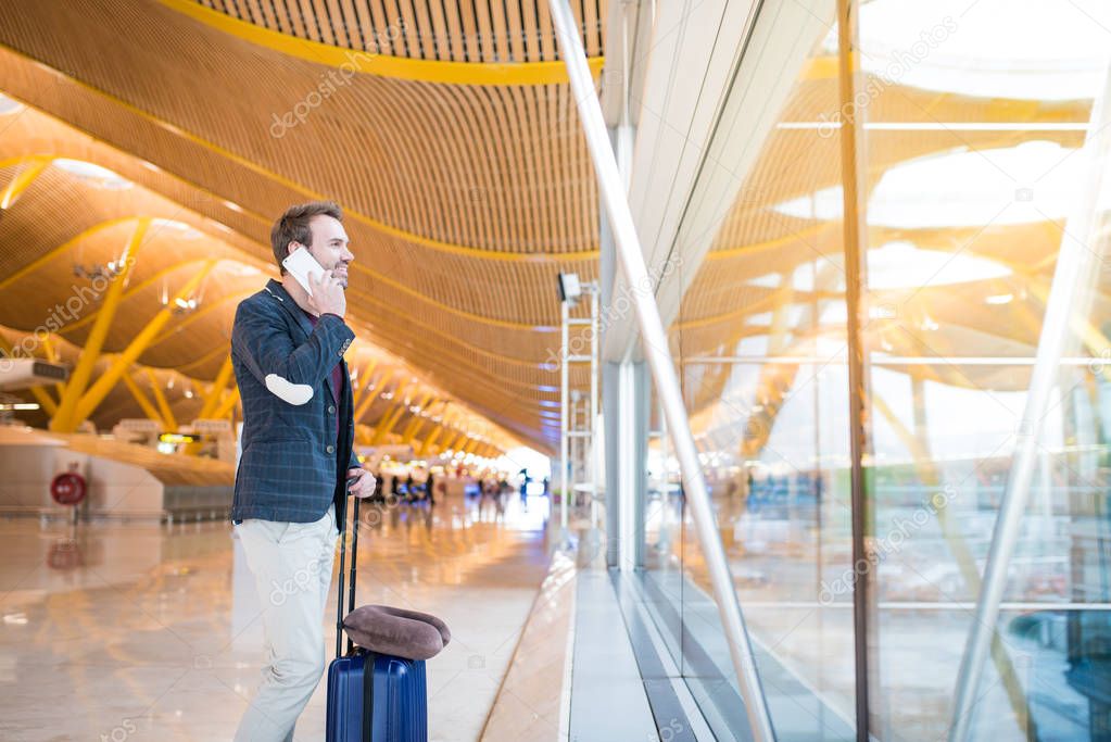 man using mobile phone at the airport looking trough the window