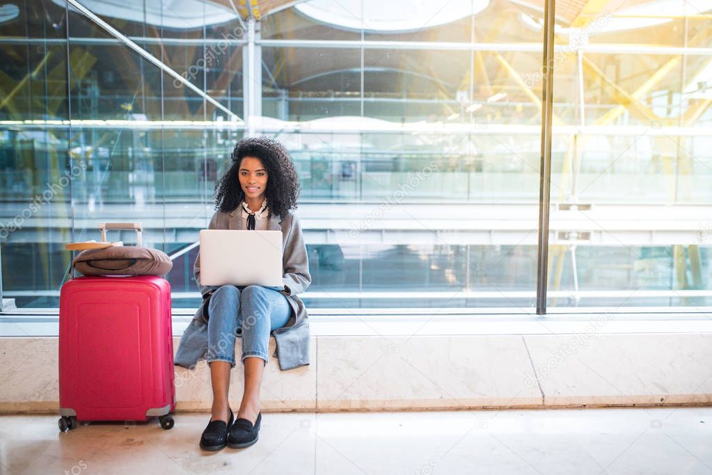 black woman working with laptop at the airport waiting at the wi