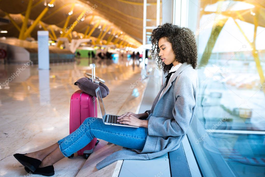 black woman working with laptop at the airport waiting at the wi