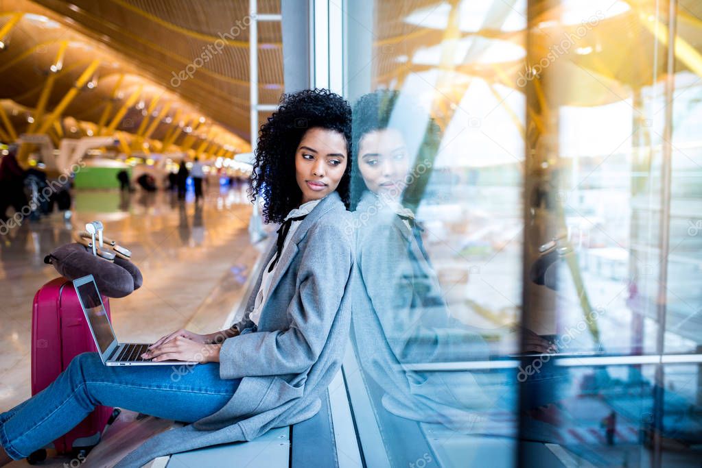 black woman working with laptop at the airport waiting at the wi