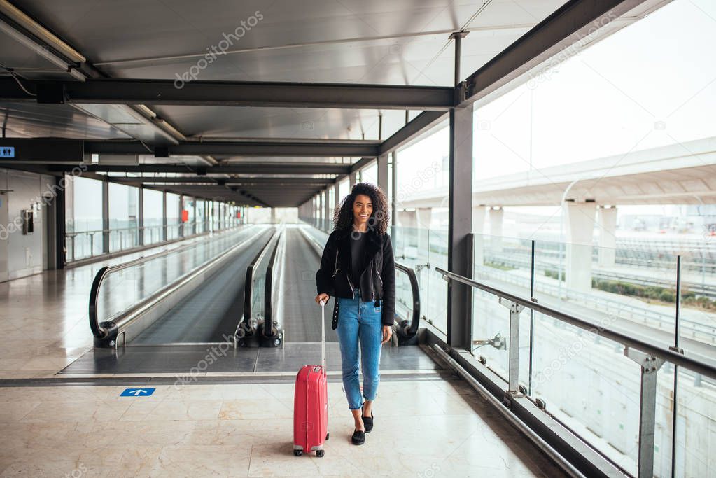 woman in the moving walkway at the airport with a pink suitcase.