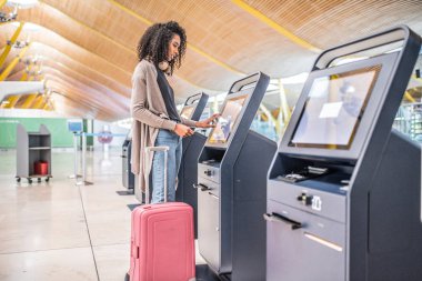 check-in makinesini biniş kartı almak havaalanında kullanan mutlu siyah kadın.