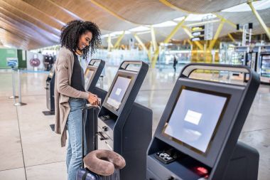 check-in makinesini biniş kartı almak havaalanında kullanan mutlu siyah kadın.