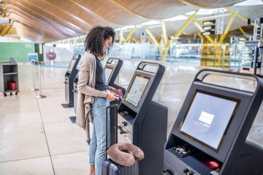 check-in makinesini biniş kartı almak havaalanında kullanan mutlu siyah kadın.