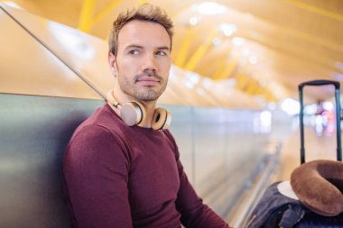 Bekleyen müzik dinleme ve bavulla havaalanında cep telefonuyla genç adam