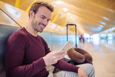 Cep telefonuyla bavulla havaalanında bekleyen genç adam