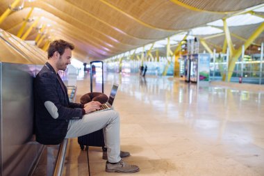 Diz üstü uçağını bavulla bekleyen çalışma Havaalanı'nda oturan genç çekici adam.