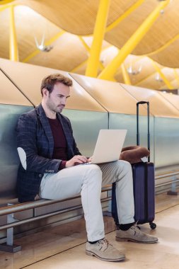 Diz üstü uçağını bavulla bekleyen çalışma Havaalanı'nda oturan genç çekici adam.