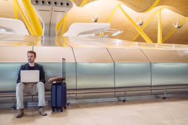 Diz üstü uçağını bavulla bekleyen çalışma Havaalanı'nda oturan genç çekici adam.