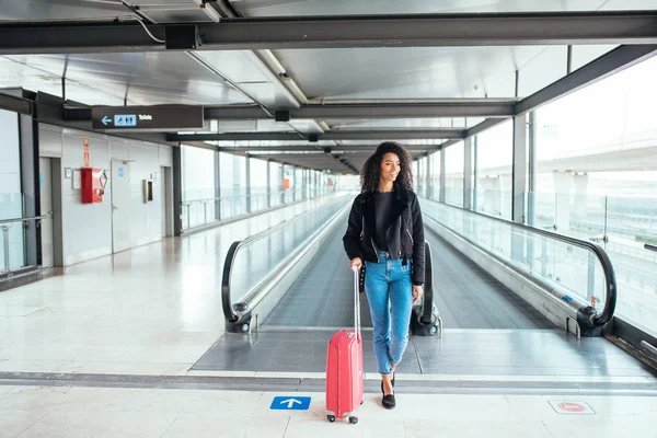 Mulher na passarela em movimento no aeroporto com uma mala rosa . — Fotografia de Stock