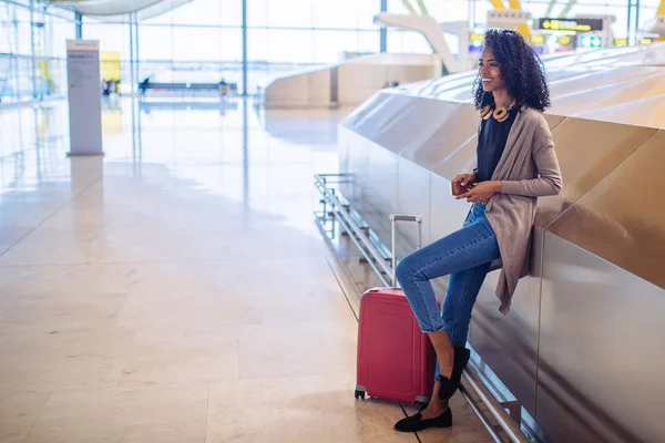 Czarny Kobieta czeka jej lotu za pomocą telefonu komórkowego na lotnisku — Zdjęcie stockowe