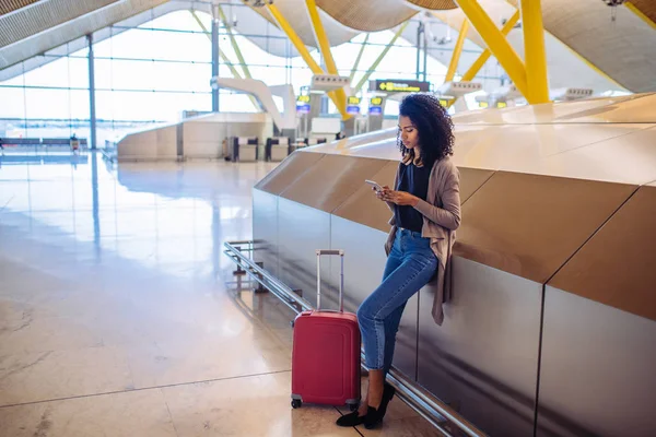 Frau wartet am Flughafen mit Handy auf ihren Flug — Stockfoto