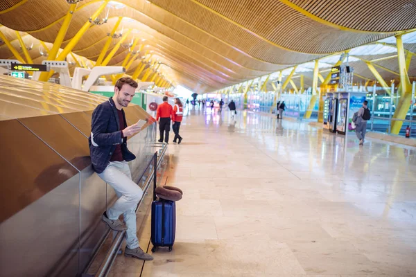 若い男、空港で待っていると使用しての携帯電話 — ストック写真