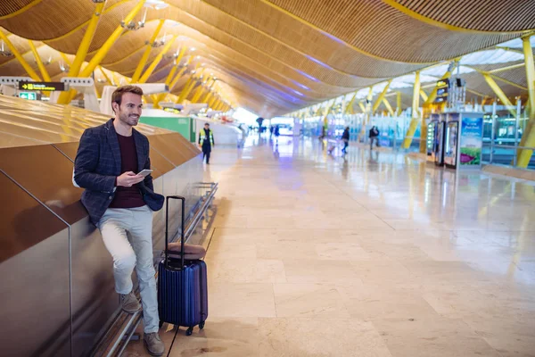 Junger Mann wartet und benutzt Handy am Flughafen — Stockfoto