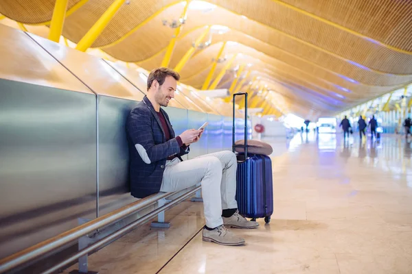 Junger Mann wartet und benutzt Handy am Flughafen — Stockfoto